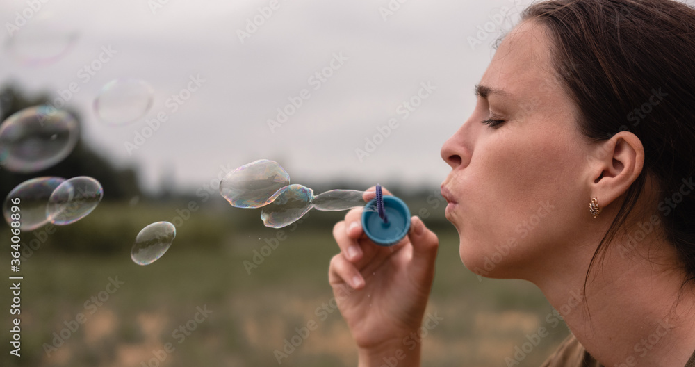 The girl blows soap bubbles. A young woman sits in nature and blows soap balls. Face in profile.