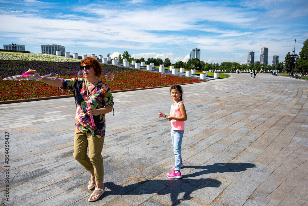 Fototapeta premium grandmother and beautiful girl who poses with soap bubbles in the park