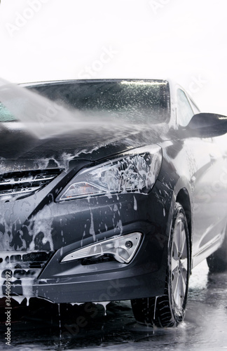 Detergent is washed off the front of a gray car with water