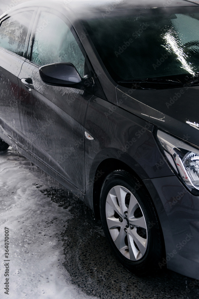 Detergent is washed off with water from the side of the gray car at the sink