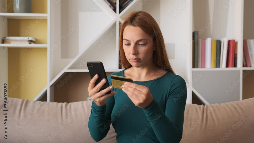 Young woman customer holding credit card and smartphone sitting on couch at home. Happy female shopper using instant easy mobile payments making purchase in online store. E-banking app service Young woman customer holding credit card and smartphone sitting on couch at home. Happy female shopper using instant easy mobile payments making purchase in online store. E-banking app service