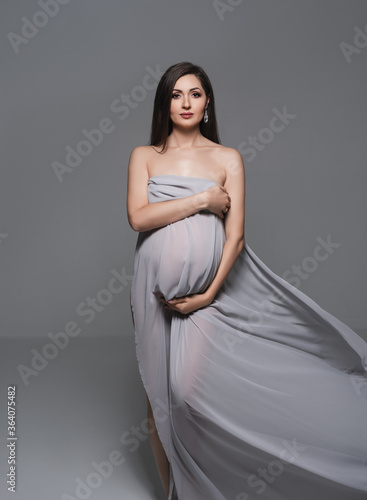 Pregnant woman wrapped in veil holding her belly with arms.Fashion portrait of happy pregnant woman.Pregnant woman wrapped in ve, maternity, preparation and expectation concept. Close-up, copy space. 