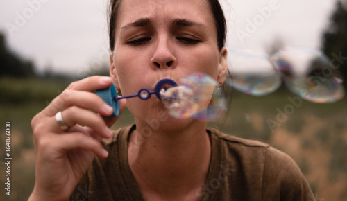 The girl blows soap bubbles. A young woman sits in nature and blows soap balls. The face in front.