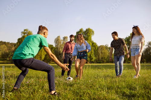 Company of friends playing football on meadow