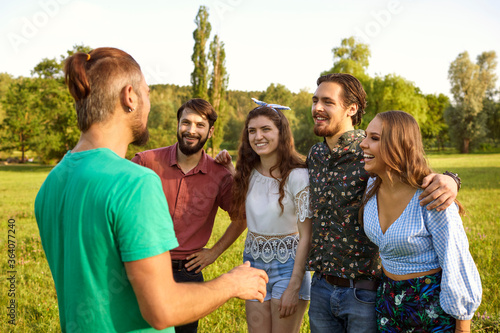 Group of joyful young people communicating outdoors on summer day. BFFs having fun times together in countryside