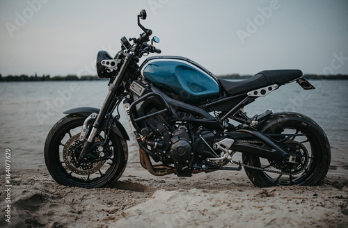 Motorcycle is on sandy beach near water.