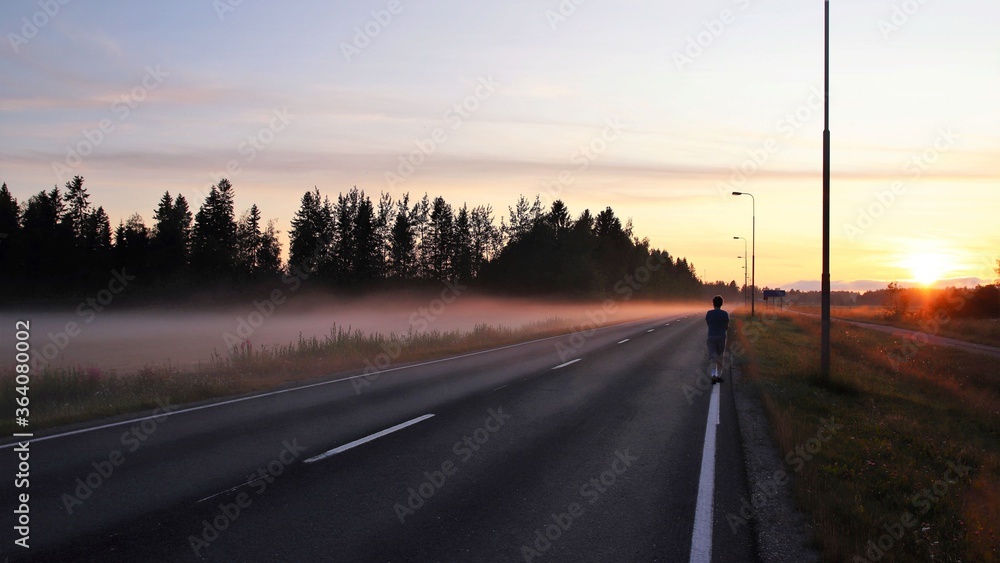A silhouette of a young teenager walking by the foggy road by himself in the evening. Concepts of solitude, teenage, growth and journey. A silhouette of a young teenager walking by the foggy road by himself in the evening. Concepts of solitude, teenage, growth and journey.