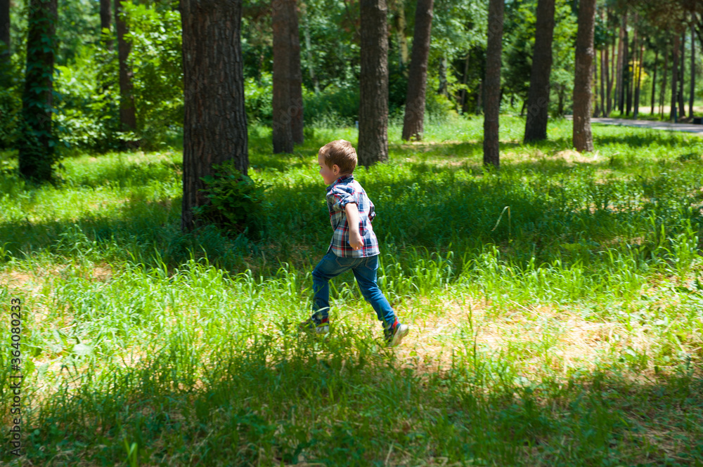 A boy running in the forest on green grass. Child have fun outdoors A boy running in the forest on green grass. Child have fun outdoors