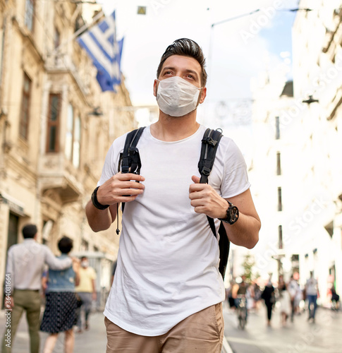 Young man wearing surgical mask face protection on crowded street in the city walks with backpack. Crawded. Tourism photo