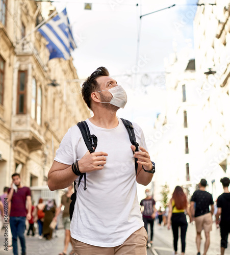 Young man wearing surgical mask face protection on crowded street in the city walks with backpack. Crawded. Tourism photo