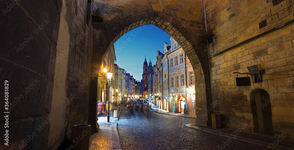 Night view of the old street of Prague thru Charles bridge tower gate