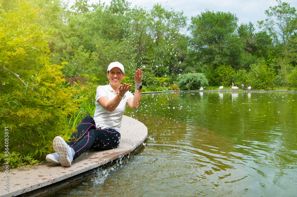 .Young blonde woman posing on a wooden pier near the lake. Girl dressed in sport trouses and white t-shirt smiling. Swan lake, outdoor. .Young blonde woman posing on a wooden pier near the lake. Girl dressed in sport trouses and white t-shirt smiling. Swan lake, outdoor.