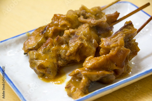トロトロに牛すじを柔らかく下処理し、串刺しにし、甘めの白味噌で煮込んだ道頓堀の大衆酒場の名物のどて焼き（どて煮）を長方形の白い皿に3本盛り付けた様子。もつ煮込み。味噌煮込み。ホルモン。