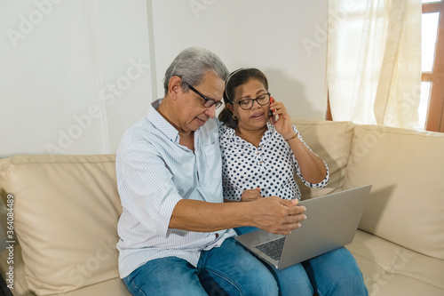 Older Latino web-surfing couple with laptop and cell phone. Two smiling older Latinas sharing and looking at the laptop - older couple with modern technology