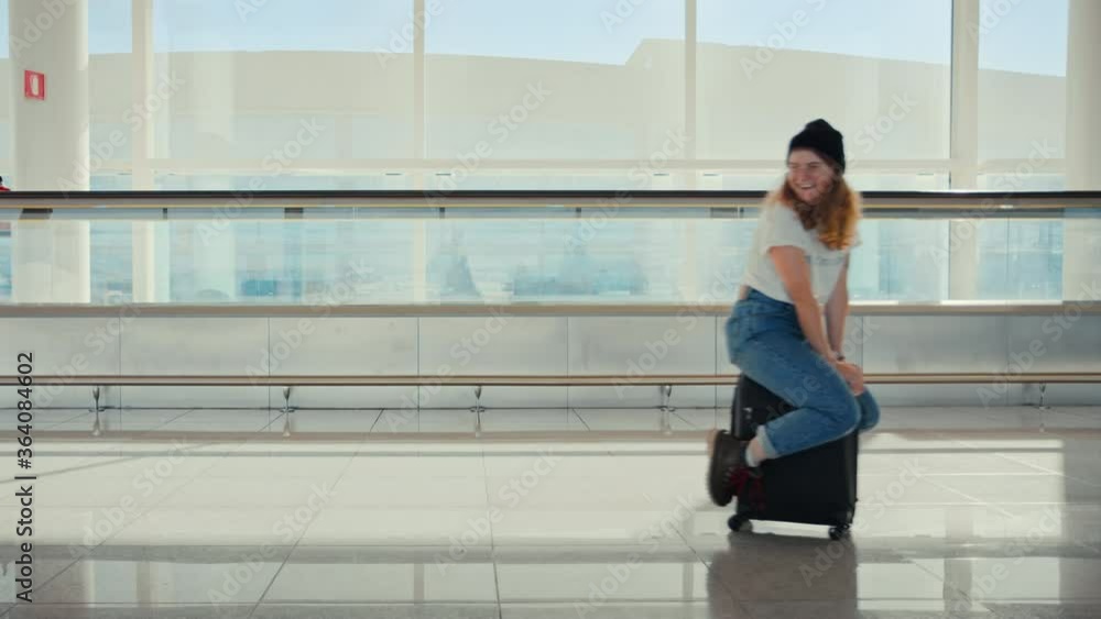 Laughing and smiling young woman ride on top of suitcase in airport. Jokes and fun millennial traveller have best time waiting for departure flight. Exciting trip destination Laughing and smiling young woman ride on top of suitcase in airport. Jokes and fun millennial traveller have best time waiting for departure flight. Exciting trip destination