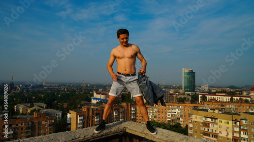 A smart guy in a unbuttoned shirt on the roof at the dawn