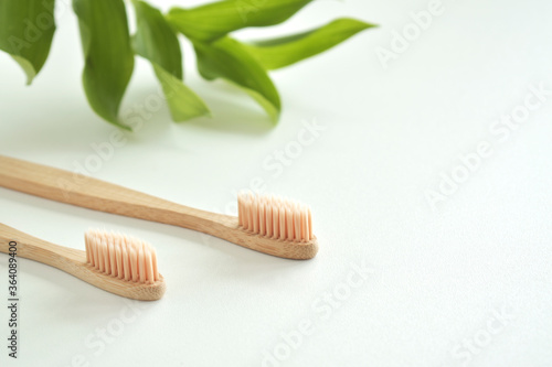 Bamboo toothbrush on a white background and green leaves. Biodegradable personal care products. No plastic