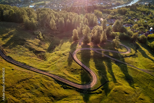 Beautiful curvy country road with fir trees in background during the sunrise with rays of light. Comanesti, Romania.