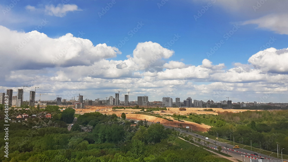 Panorama of the city with parks from a height. Blue sky with clouds on buildings under construction.