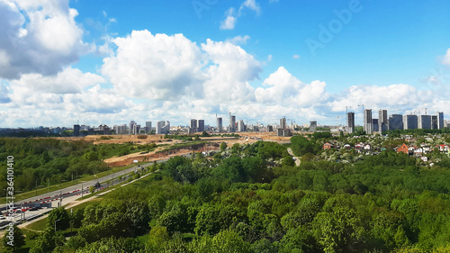 Panorama of the city with parks from a height. Blue sky with clouds on buildings under construction.