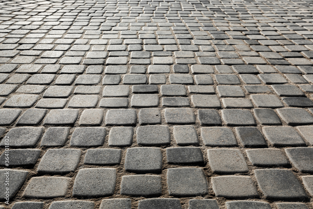 The surface is paved with road tiles of different sizes (multi format). The uneven (melange) color of the tile makes it look like a natural stone. Perspective viewpoint.