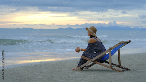 Asia woman sitting on beach chair and enjoying during the sunset on the beach. Summer vacation concept. © Jera