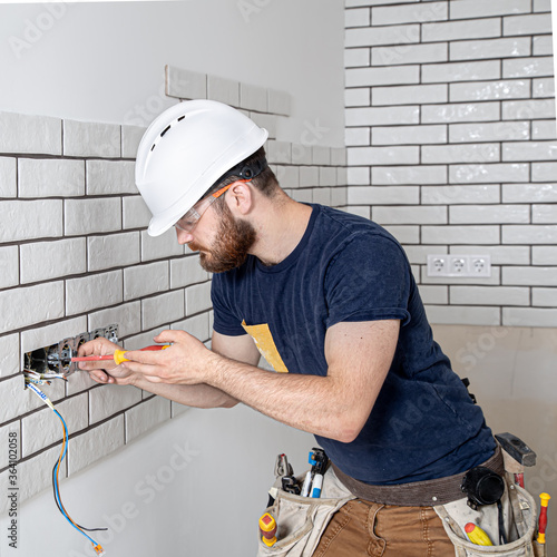 Electrician Builder at work, installation of sockets and switches. Professional in overalls with an electrician's tool. Against the background of the repair site.