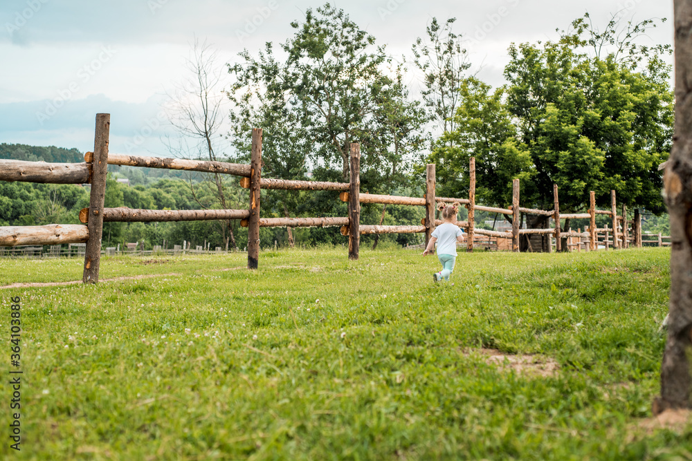 Lifestyle, baby girl running about the wooden fence, summer day on the forest background. Vocation in the village. Sun and sunset. Lifestyle, baby girl running about the wooden fence, summer day on the forest background. Vocation in the village. Sun and sunset.