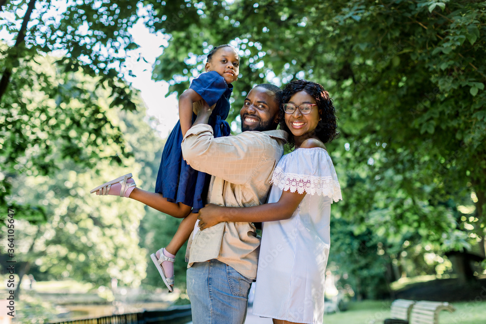 Happy joyful young African family, father, mother and little daughter, having fun outdoors, playing together in summer park. Mom, dad and kid laughing, enjoying nature outside Happy joyful young African family, father, mother and little daughter, having fun outdoors, playing together in summer park. Mom, dad and kid laughing, enjoying nature outside