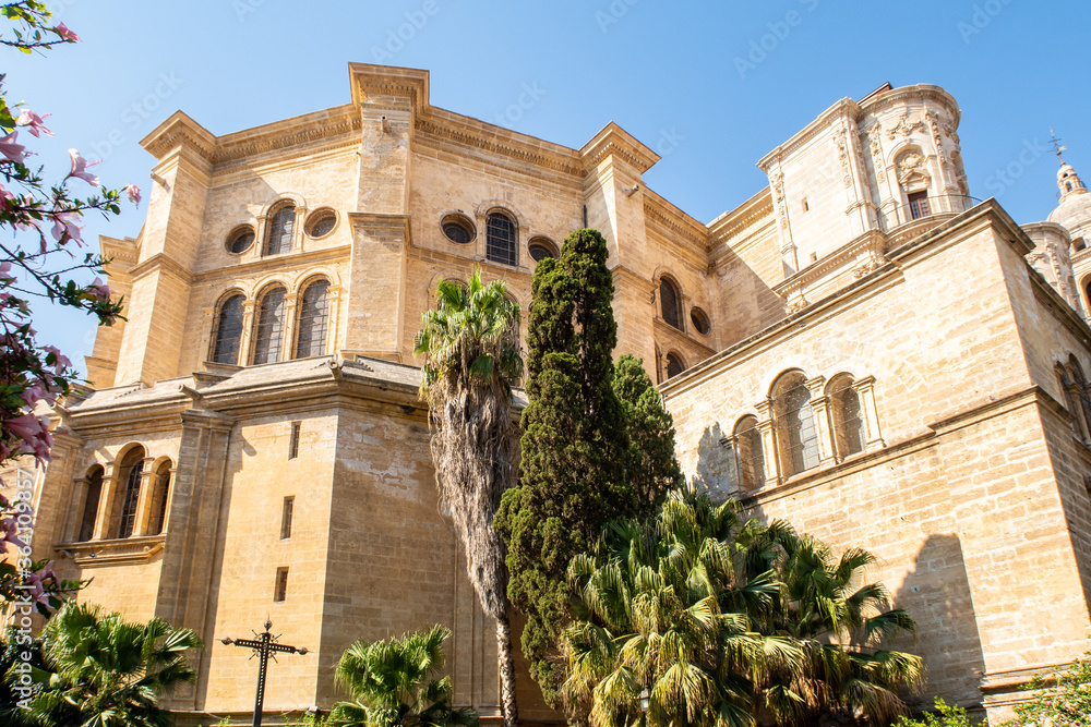 Fototapeta premium The Cathedral of Malaga back view from Calle Cister street. Medieval Roman Catholic church in renaissance style with baroque facade, green trees and a garden in front. Malaga, Andalusia,Spain.