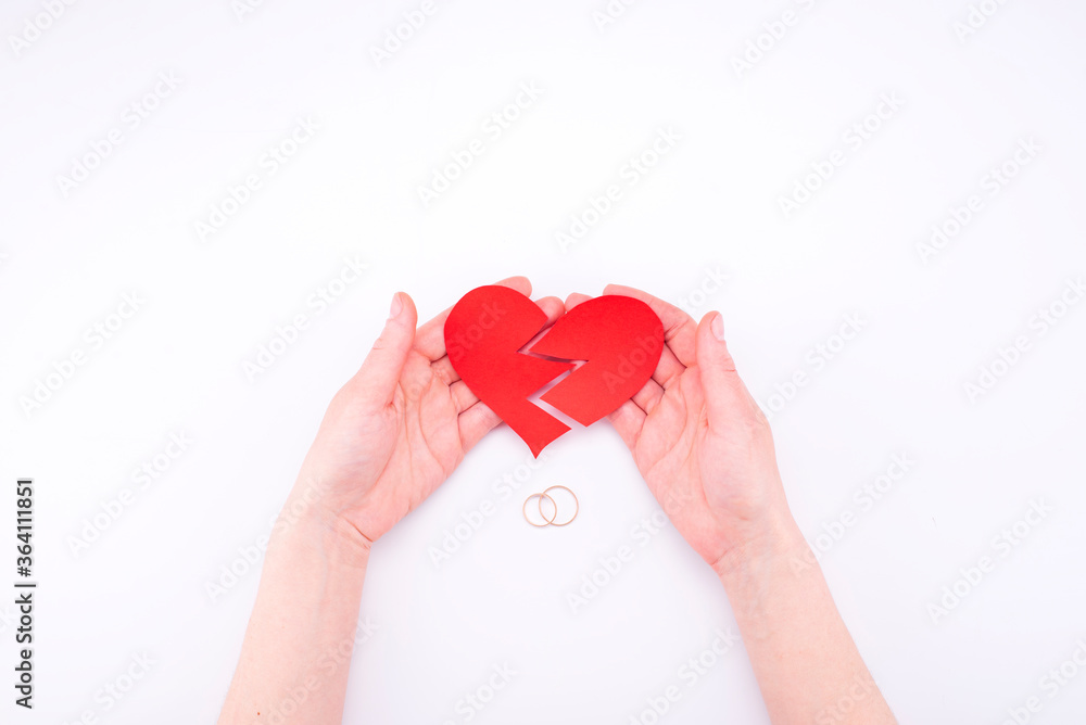 Fototapeta premium Female hands hold a broken heart on a white background with wedding rings. Relationship problems in marriage, divorce