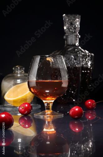 Glass of cognac, cherry, lemon and decanter on a dark background