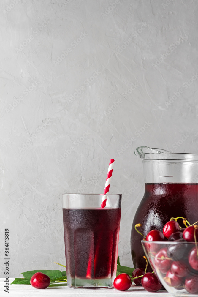Cherry juice in a glass with a straw and jug with fresh berries on white background. Refreshment summer drink Cherry juice in a glass with a straw and jug with fresh berries on white background. Refreshment summer drink