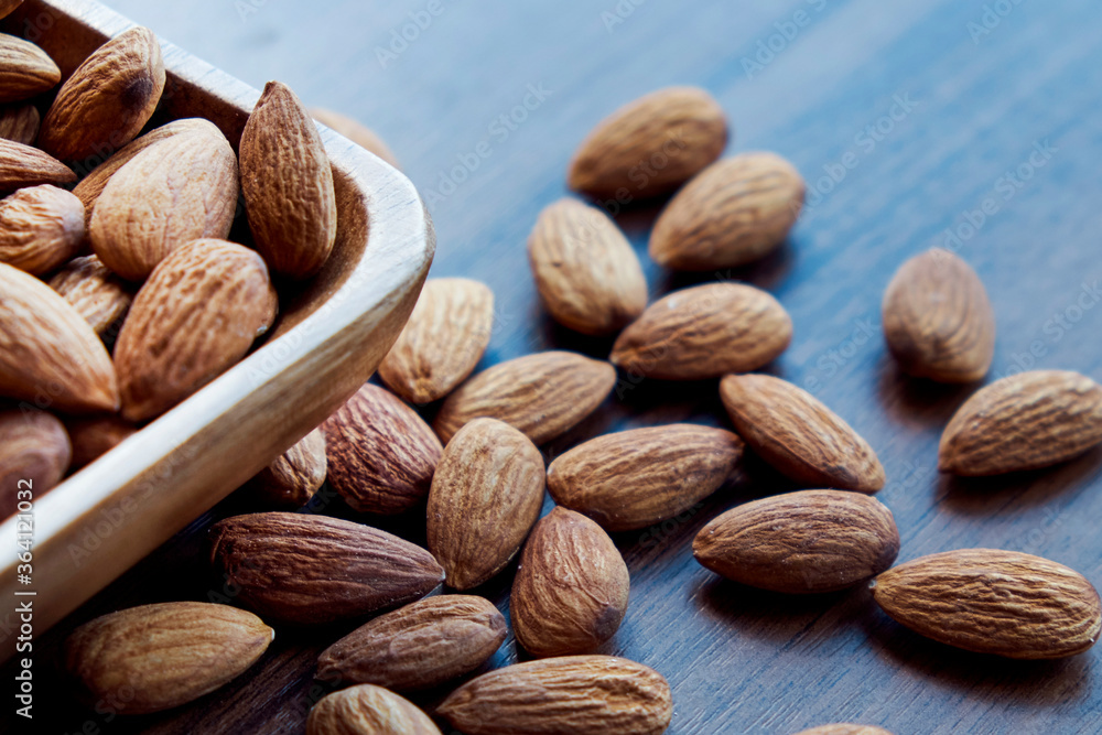 Almonds in small wooden bowl. Almonds laid freely on dark table. Row of bowls with almond nuts, top view. Peeled almond pattern Almonds in small wooden bowl. Almonds laid freely on dark table. Row of bowls with almond nuts, top view. Peeled almond pattern
