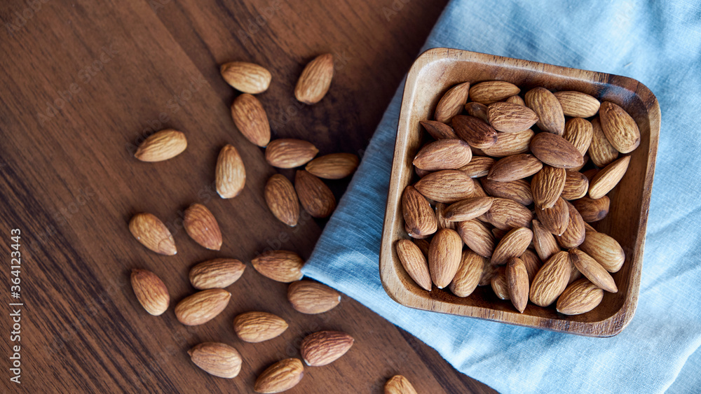 Almonds in small wooden bowl. Almonds laid freely on dark table. Row of bowls with almond nuts, top view. Peeled almond pattern Almonds in small wooden bowl. Almonds laid freely on dark table. Row of bowls with almond nuts, top view. Peeled almond pattern