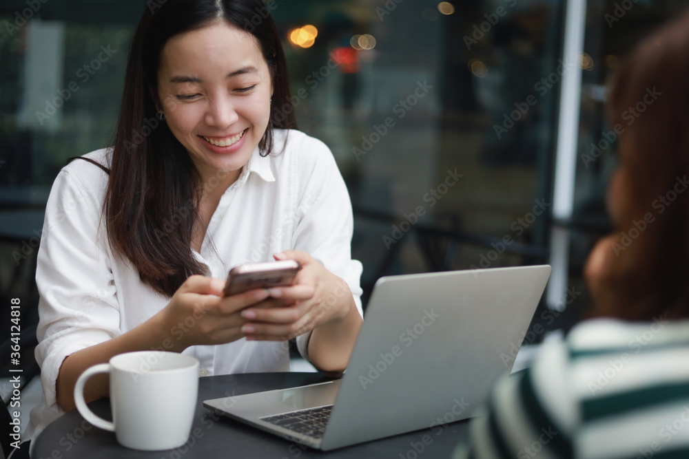 Asian woman working with computer laptop and drinking coffee in coffee shop cafe smile and happy face and talking with friend Asian woman working with computer laptop and drinking coffee in coffee shop cafe smile and happy face and talking with friend