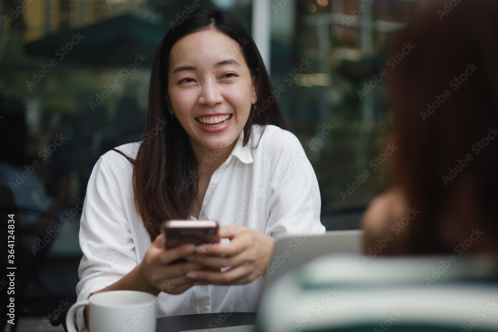 Asian woman working with computer laptop and drinking coffee in coffee shop cafe smile and happy face and talking with friend Asian woman working with computer laptop and drinking coffee in coffee shop cafe smile and happy face and talking with friend