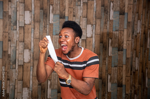 an excited young african man looking at his betting slip and looking surprised and happy, celebrating photo