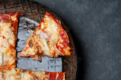 Slice of a fresh Pizza in an rustic iron Pan on a Slate Plate. Close up.
