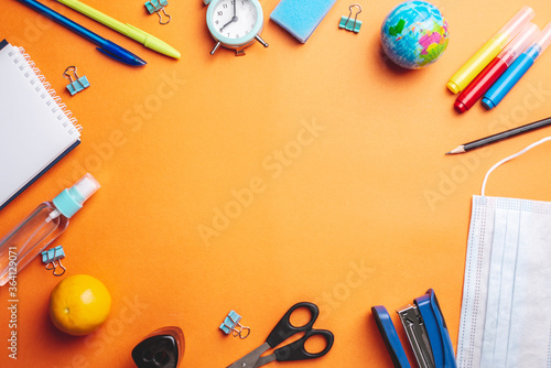 Stationery school supplies, medical mask and antiseptic on a orange background. Copy space. Concept of back to school