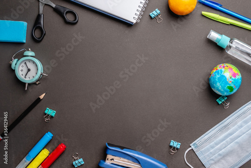 Stationery school supplies, medical mask and antiseptic on a black background. Copy space. Concept of back to school photo