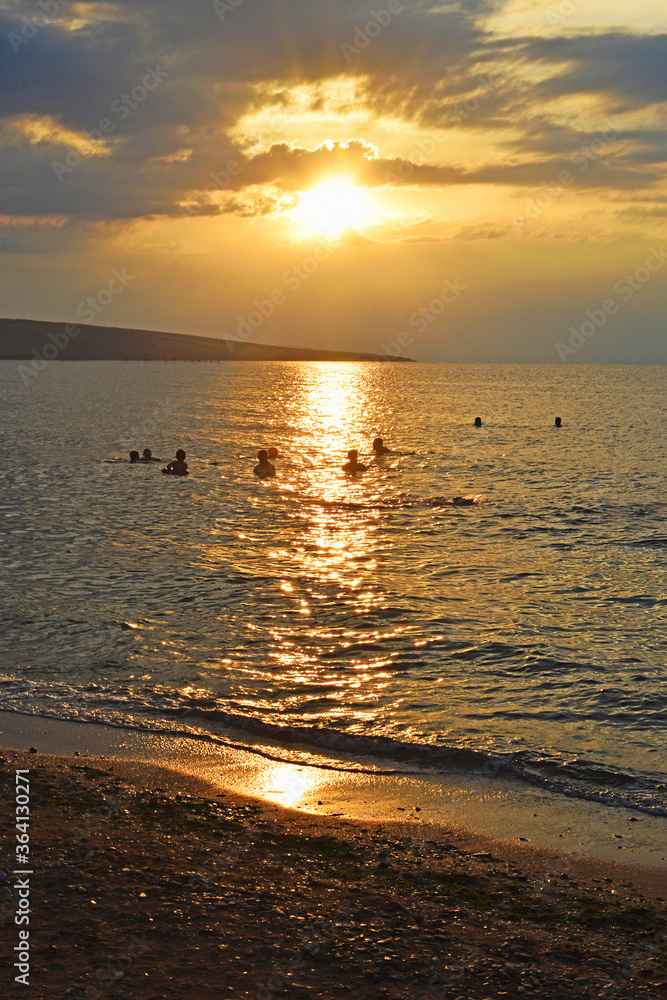 Silhouettes of people in the sea at sunset