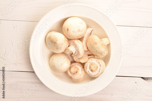 Freshly cut mushrooms on a plate, close-up, on a white wooden table.