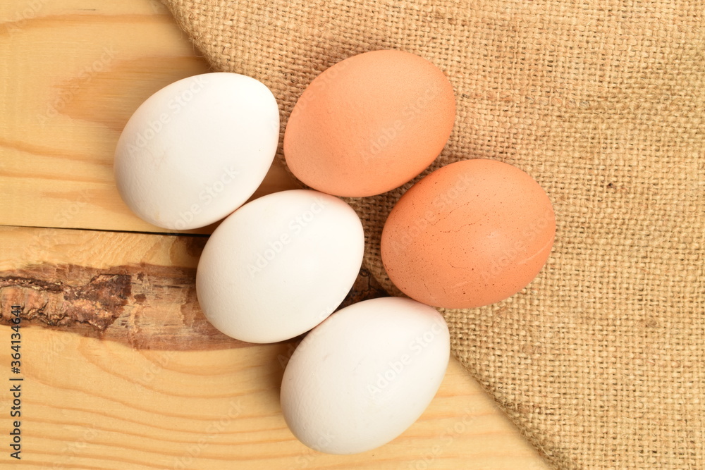 Several chicken eggs with a jute napkin, in a basket, close-up, on a wooden table. Several chicken eggs with a jute napkin, in a basket, close-up, on a wooden table.