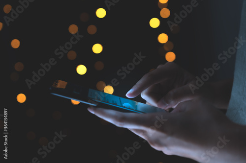 Technology business concoept: A busuness Woman serfing the internet by using a mobile in cool tone dark backgrond with bokeh warm light