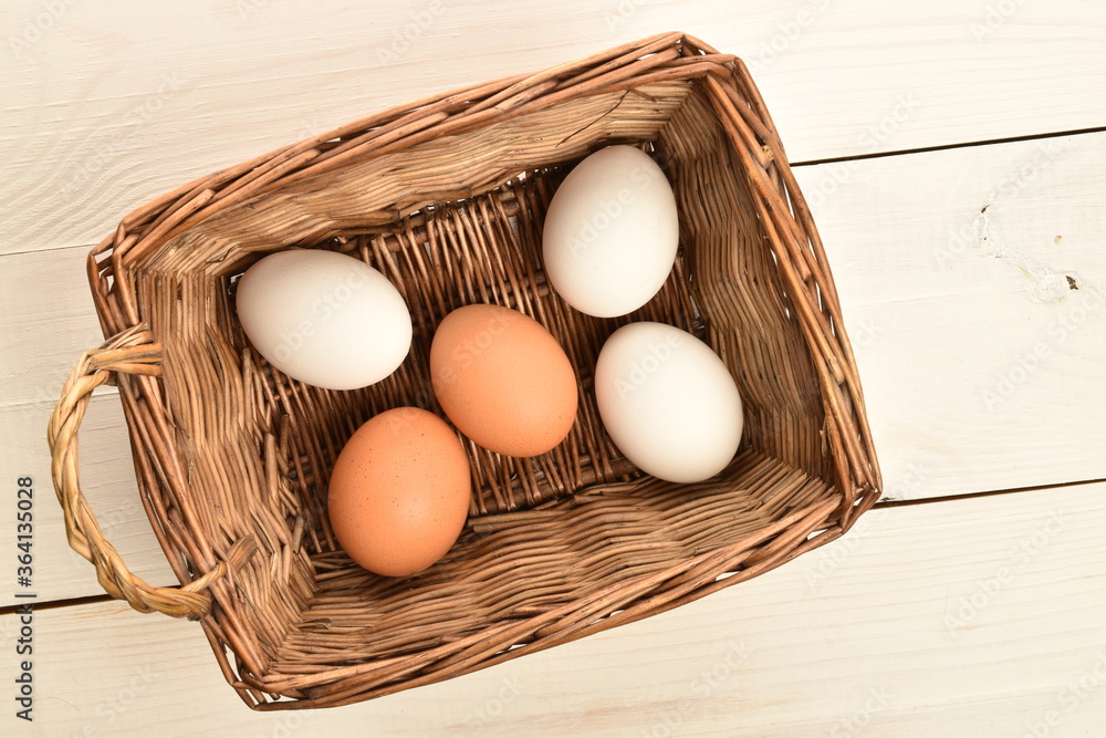 Several chicken eggs in a wicker basket, on a white wooden table. Several chicken eggs in a wicker basket, on a white wooden table.