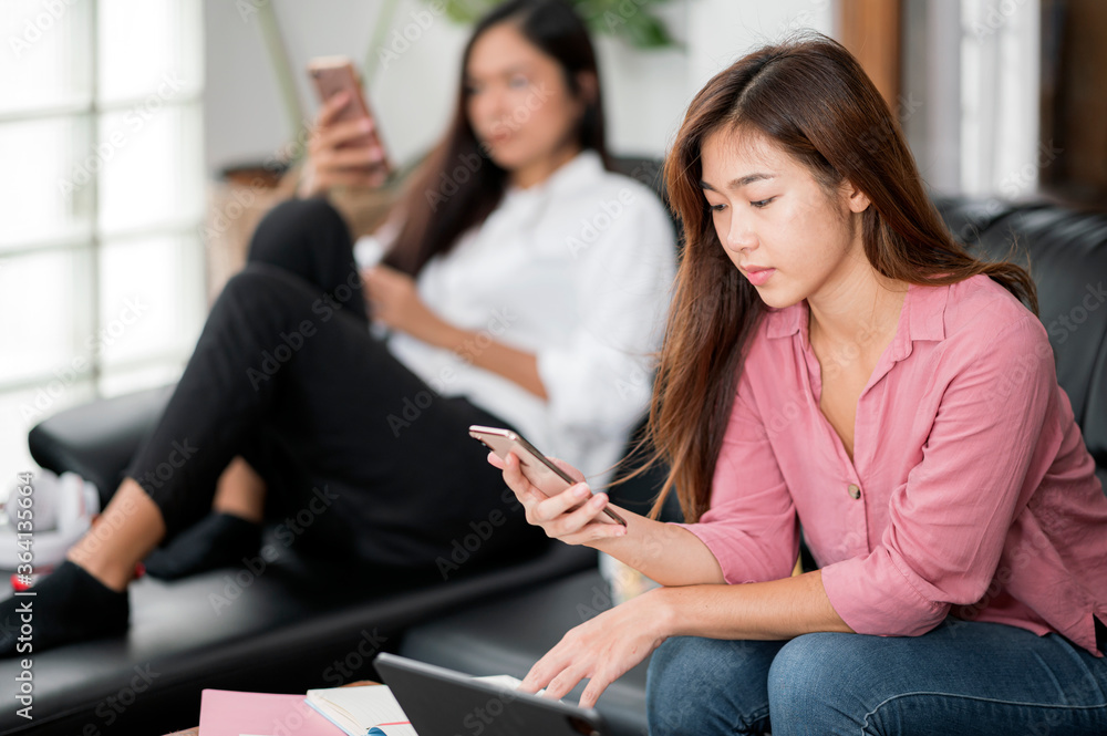 Two young asian female using smartphone whitel sitting in living room at home. Two young asian female using smartphone whitel sitting in living room at home.