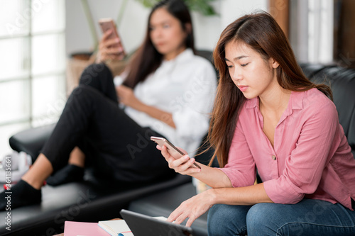 Two young asian female using smartphone whitel sitting in living room at home.