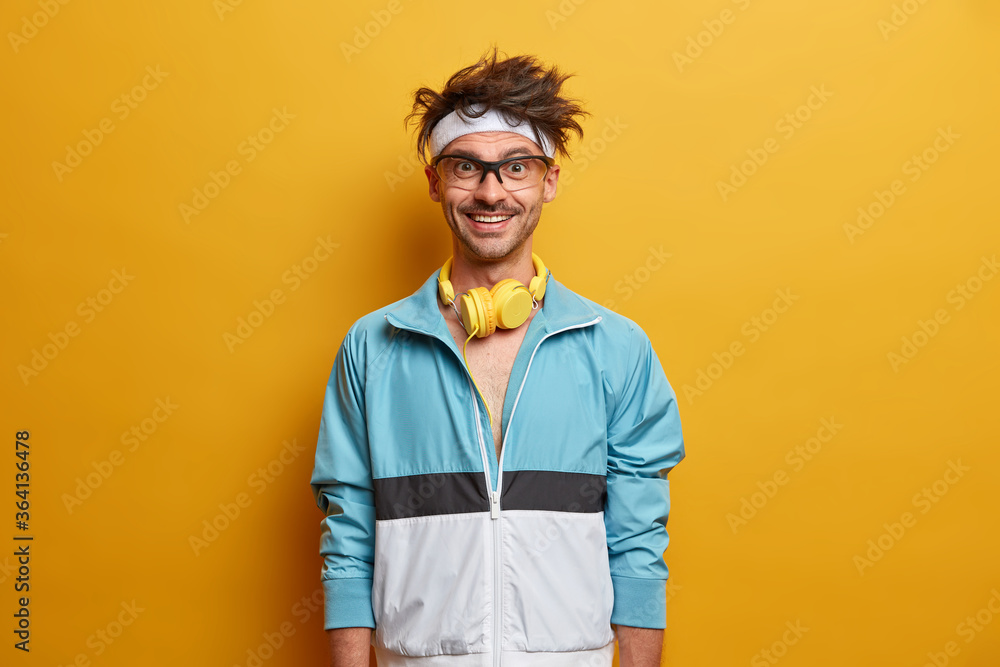 Φωτογραφία Strong sporty man with glad expression, happy to do workout, listens music in headphones, dressed in sportswear, being in good mood, wants to be strong and healthy