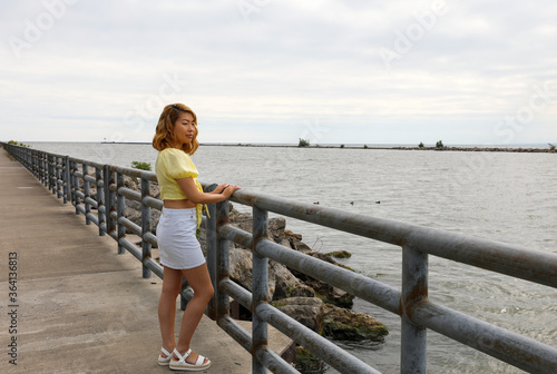 Young woman on a summer morning walk stops to enjoy the view of the water from the pier.